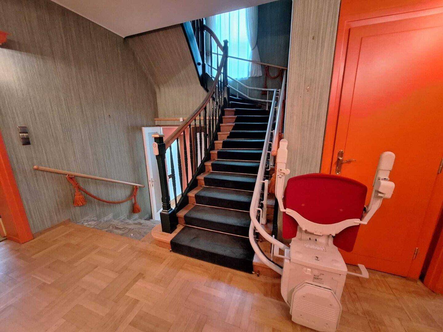 Treppenhaus mit Teppichstufen und einem Treppenlift für verbesserte Zugänglichkeit.
