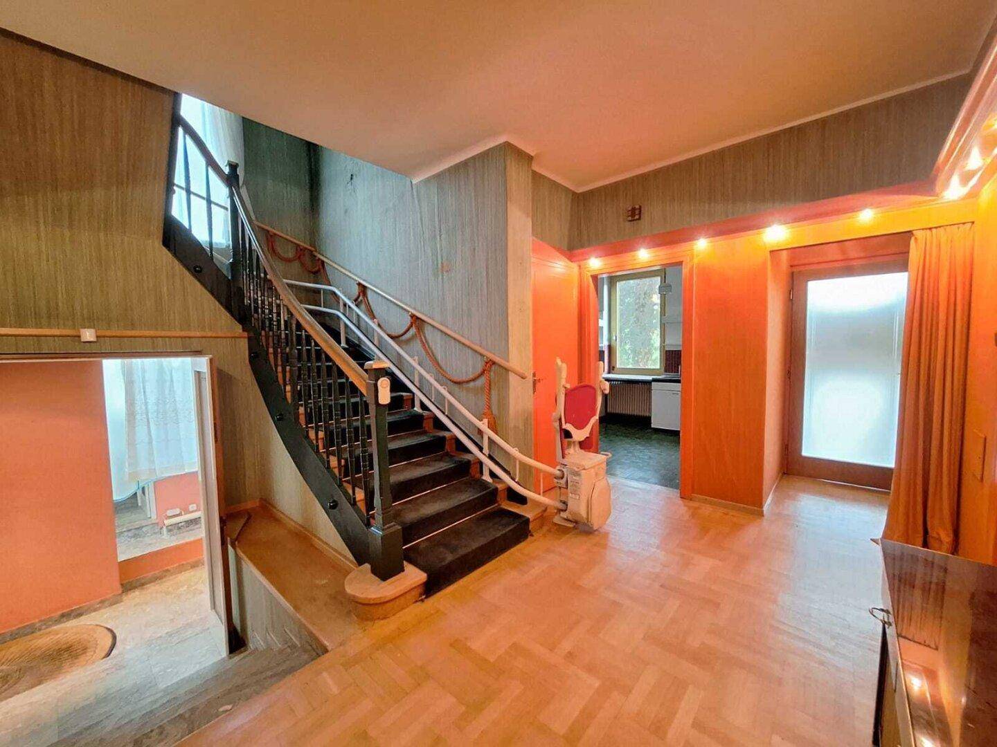Eingangsbereich mit Holzparkett, Treppe und einem Treppenlift für verbesserte Barrierefreiheit.
