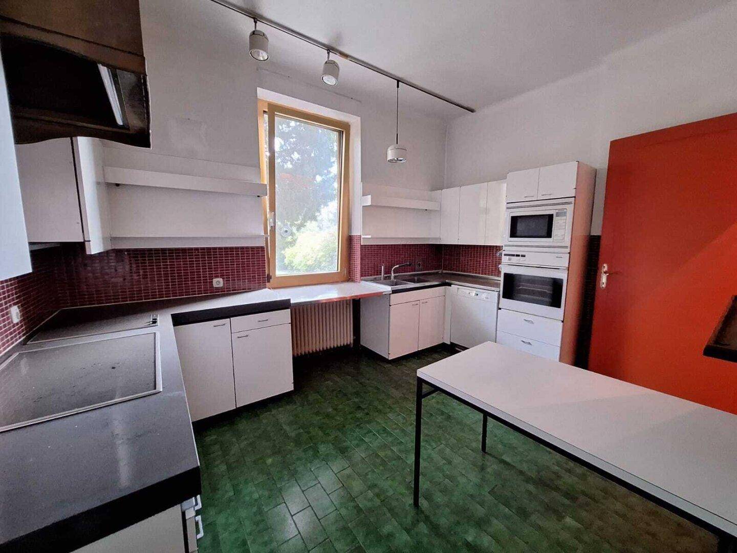Ältere Küche mit weißen Schränken, roten Fliesen und grünem Bodenbelag, bereit zur Modernisierung.