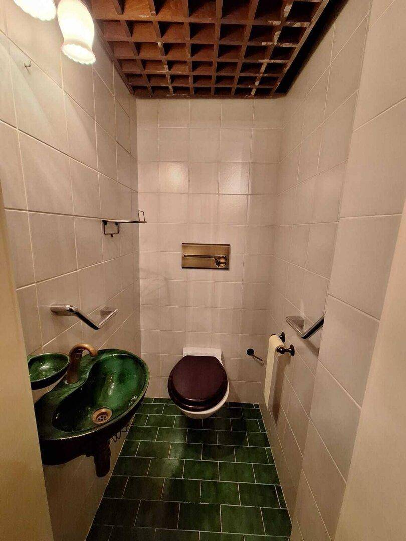 Kleines Gäste-WC mit grünem Waschbecken und Fliesenboden, im Retro-Stil.