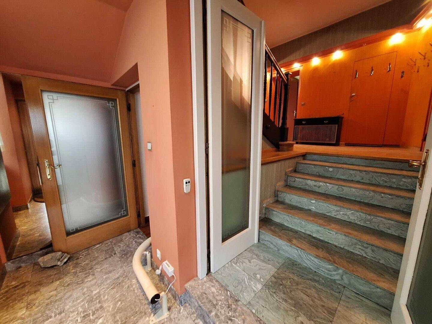 Eingangsbereich mit Marmorboden, Treppe und einem Treppenlift für verbesserte Barrierefreiheit.