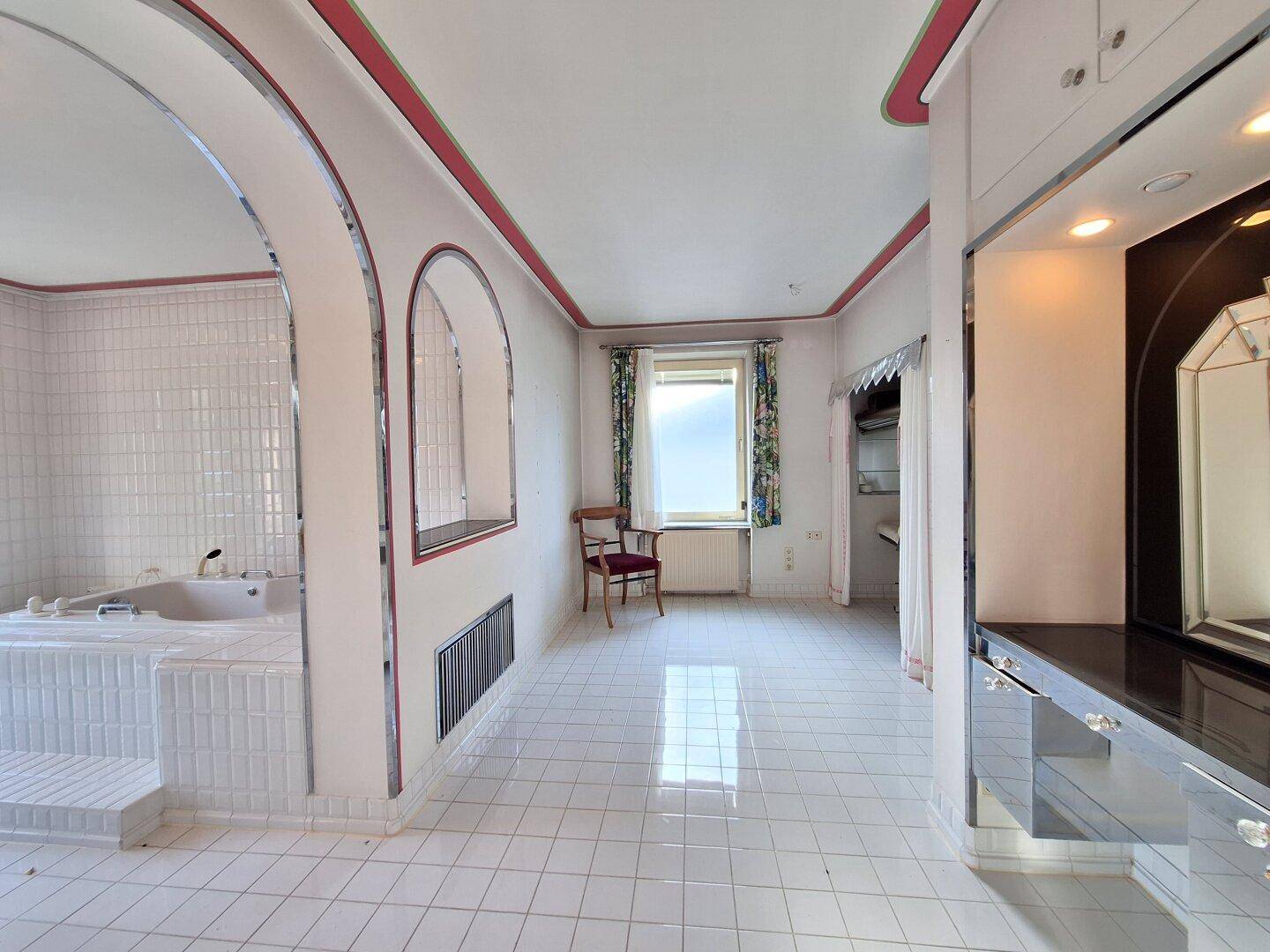 Großes Badezimmer mit weißen Fliesen, Badewanne und Zugang zu einem angrenzenden Bereich.