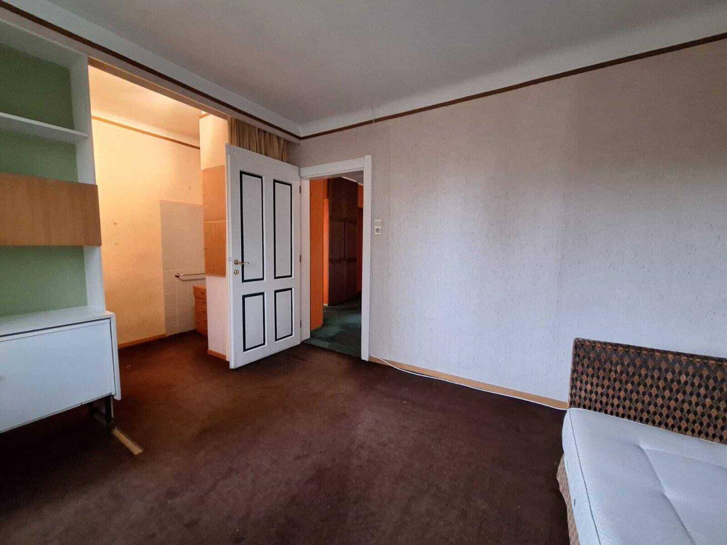 Schlafzimmer mit braunem Teppichboden, Fenster und einfacher Einrichtung, im Vintage-Stil.