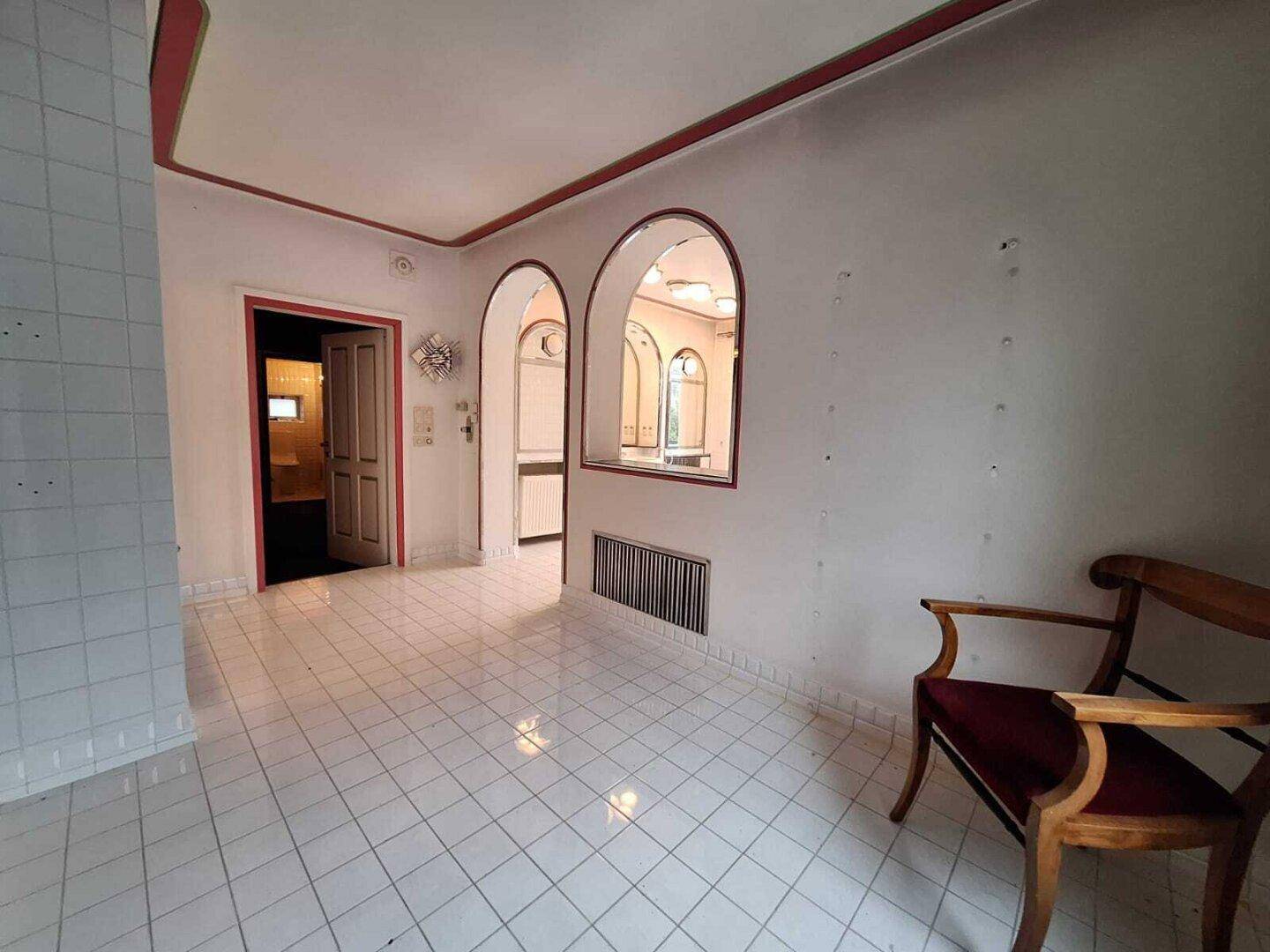 Großes Badezimmer mit weißen Fliesen, Badewanne und Zugang zu einem angrenzenden Bereich.
