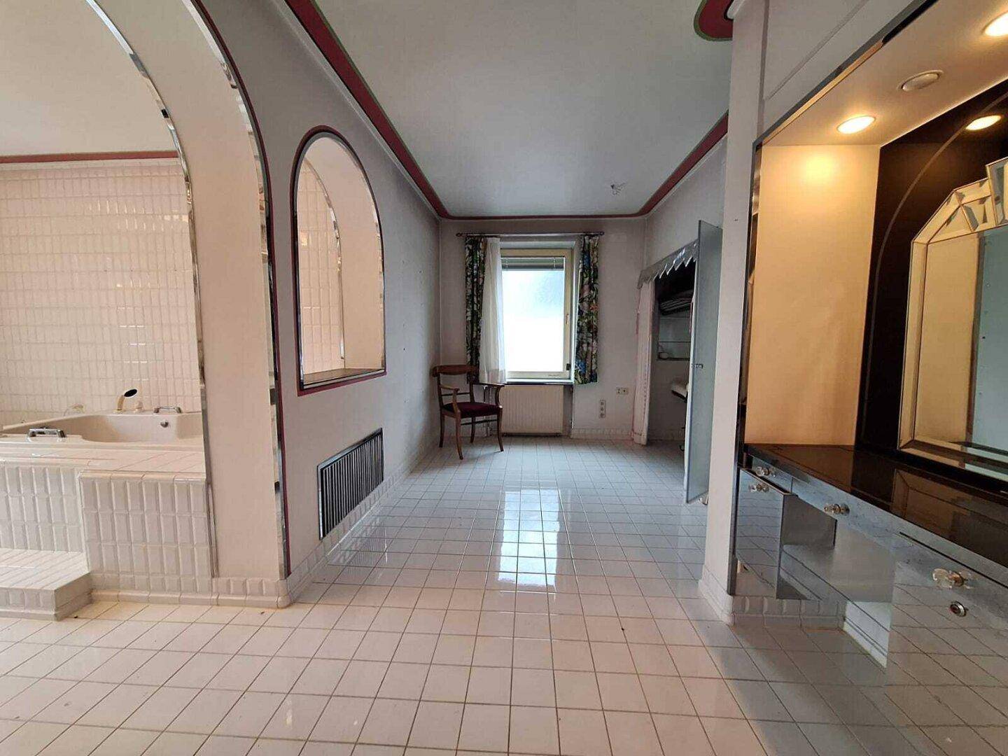 Geräumiges Badezimmer mit weißen Fliesen, Whirlpool und einem Fenster für Tageslicht.