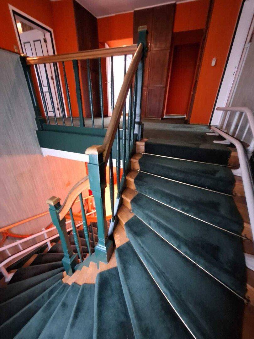 Wendeltreppe mit grünem Teppichbelag und Holzgeländer, führt nach unten, im Vintage-Stil.