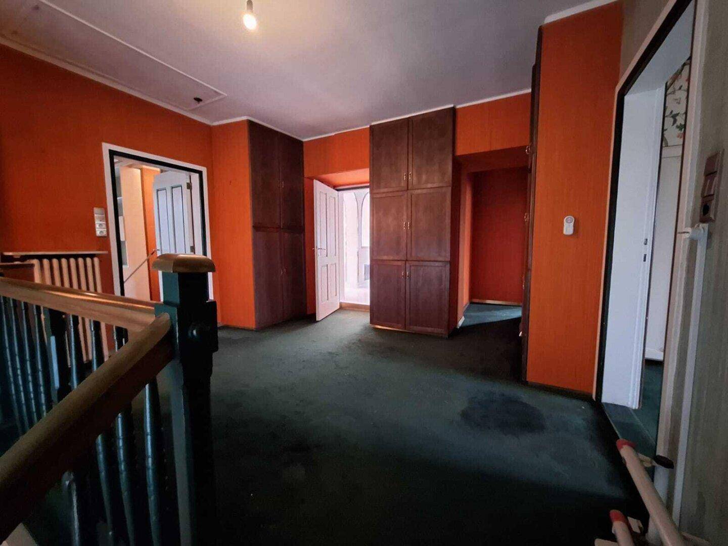 Geräumiger Flur mit orangefarbenen Wänden, dunklem Teppichboden und Einbauschränken.