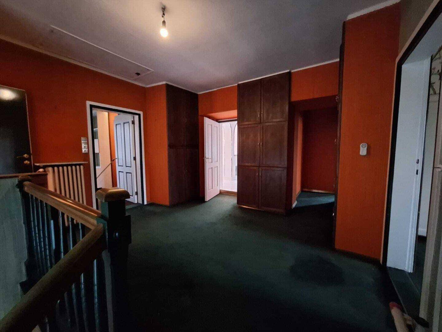 Obergeschoss-Flur mit orangefarbenen Wänden, grünem Teppichboden und praktischen Einbauschränken.