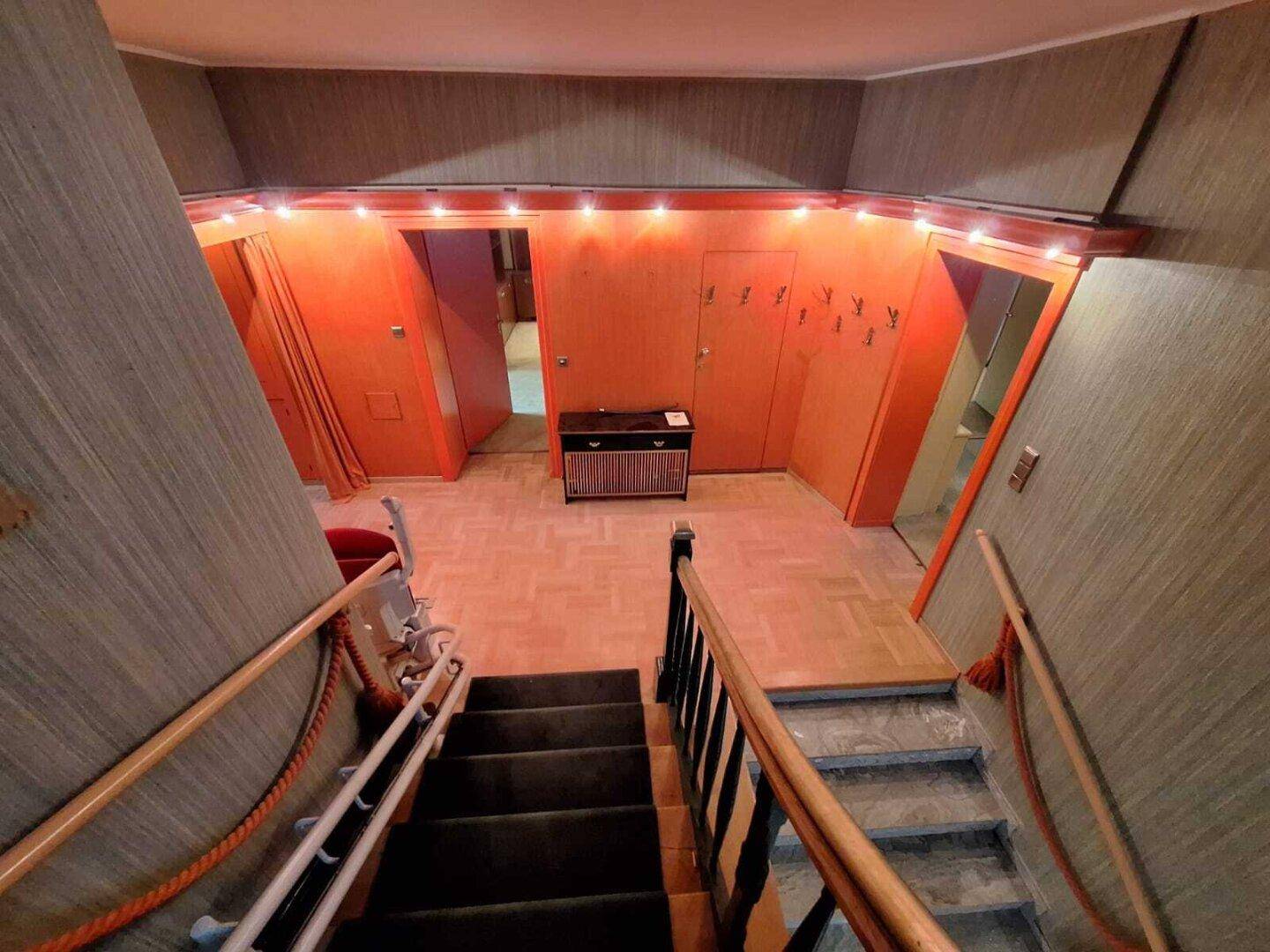 Treppenhaus mit Teppichstufen, orangefarbenen Wänden und dekorativer Beleuchtung, im Retro-Stil.