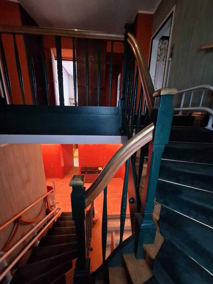 Treppenhaus mit dunklen Holzstufen, grünem Geländer und orangefarbenen Wänden im Hintergrund.