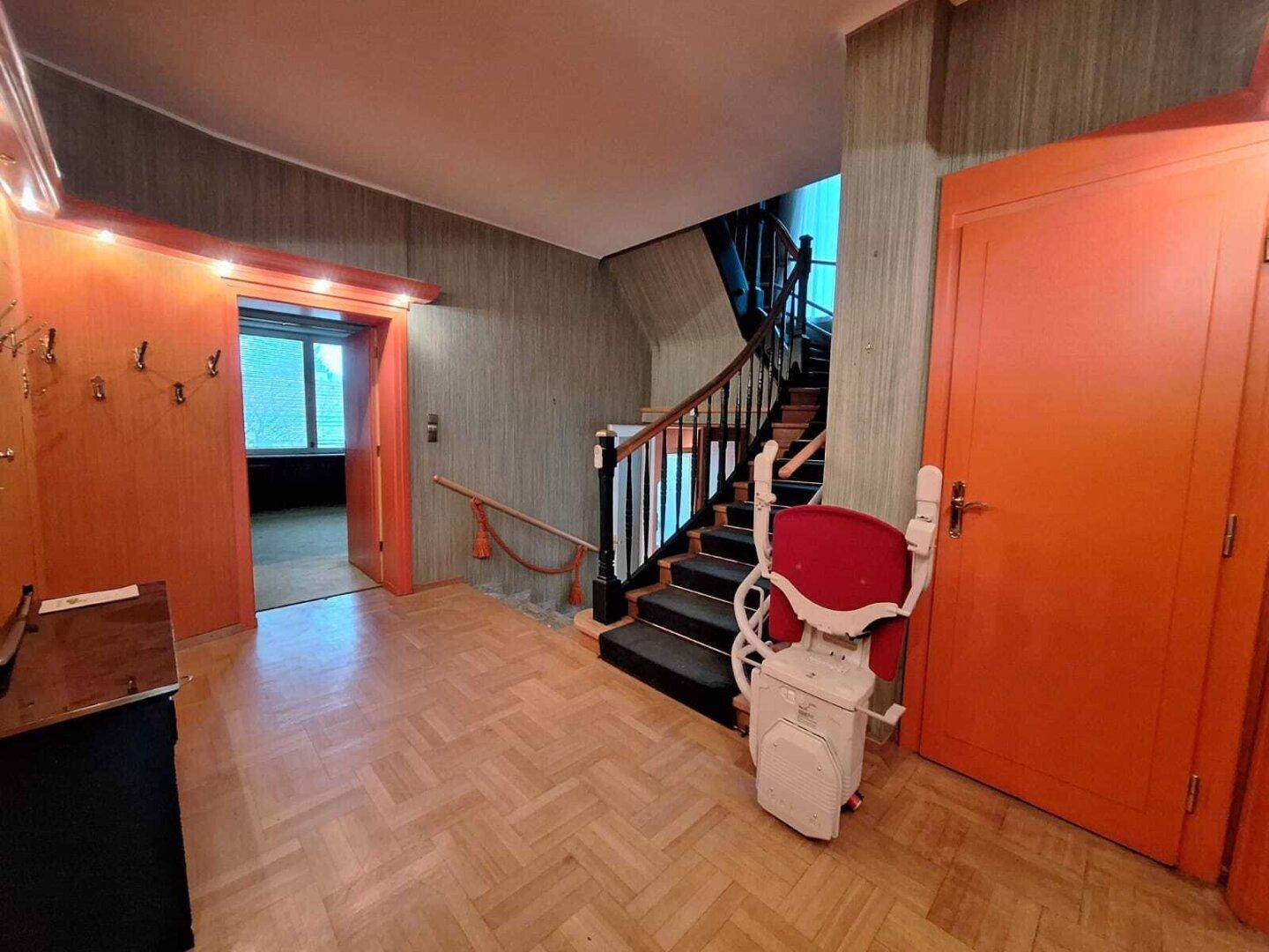 Eingangsbereich mit Holzparkett, Treppe und einem Treppenlift für verbesserte Barrierefreiheit.