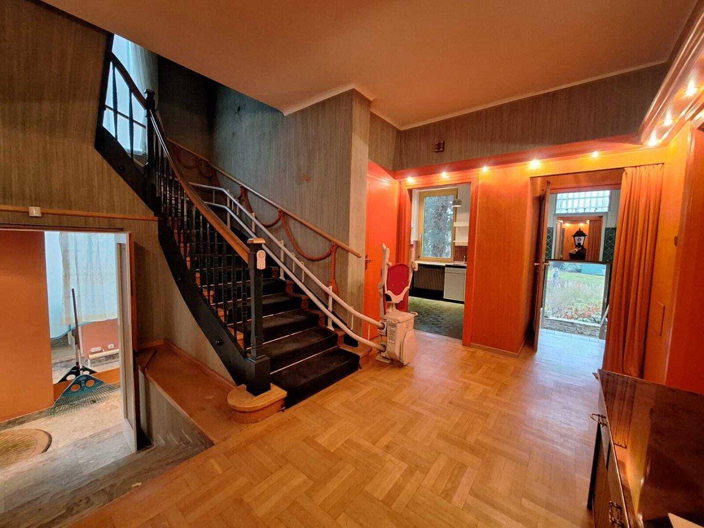 Eingangsbereich mit Holzparkett, Treppe und einem Treppenlift für verbesserte Barrierefreiheit.