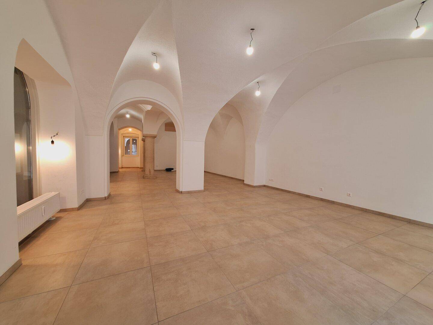 Spacious commercial area with vaulted arches, tiled flooring, and a prominent stone column, creating an elegant ambiance.