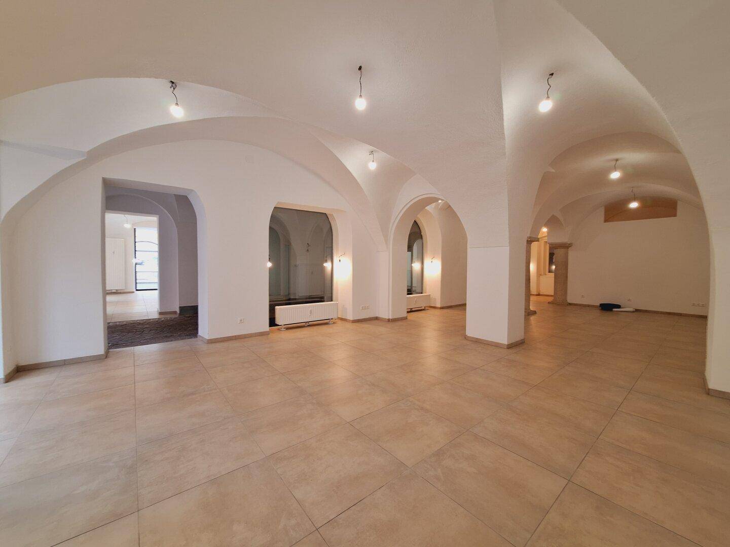 Großer, heller Gewerberaum mit eleganten Gewölbedecken, Fliesenboden und Blick auf die Straße durch die Fenster.