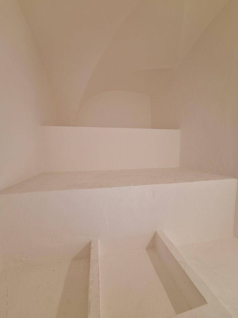 Kleiner Abstellraum unter einer Treppe mit weiß gestrichenen Wänden und einfacher Gestaltung.