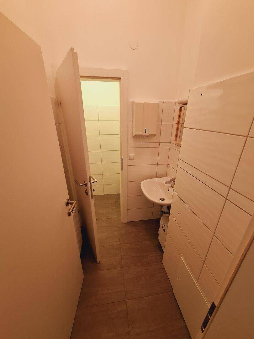 Kleiner Toilettenraum mit Waschbecken, Spiegel und hellen Wandfliesen in sauberem Zustand.