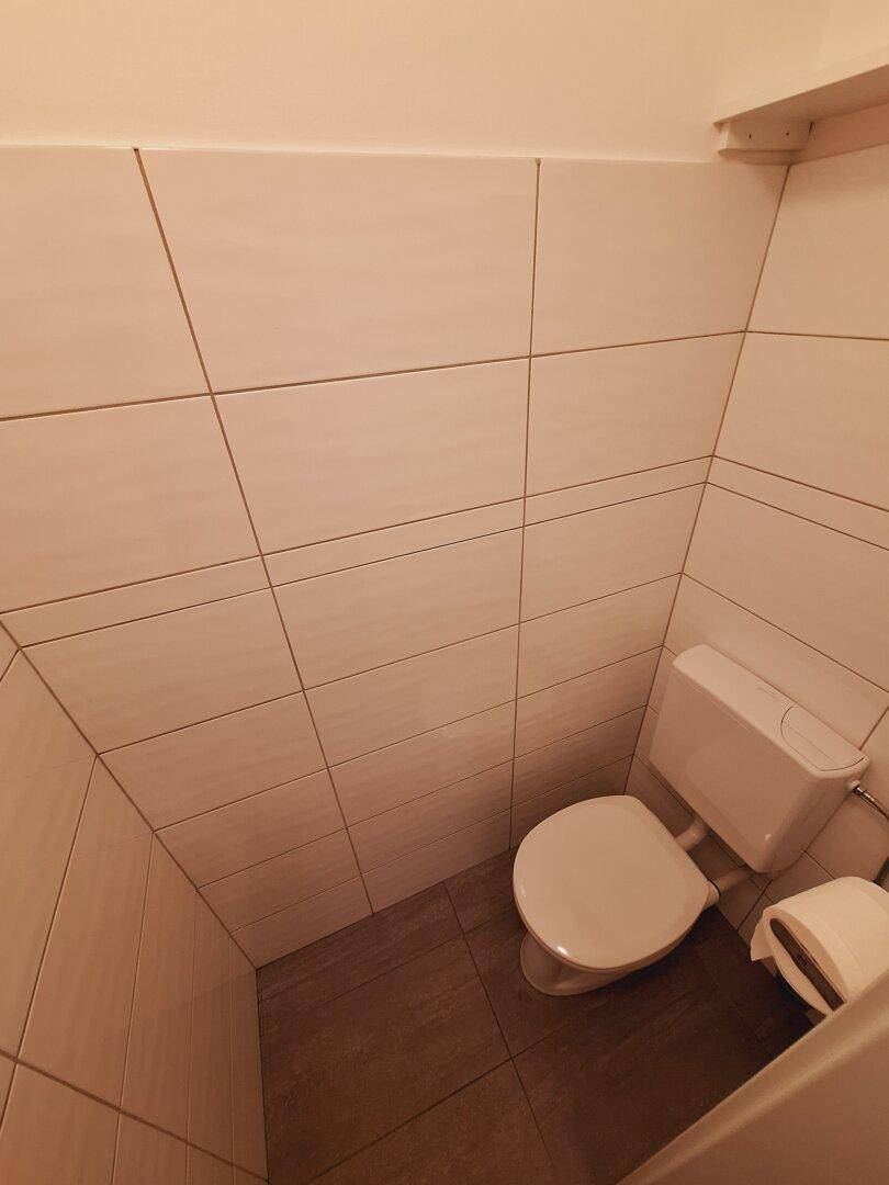 Toilettenbereich mit WC und hellen Wandfliesen, die eine saubere und funktionale Umgebung bieten.