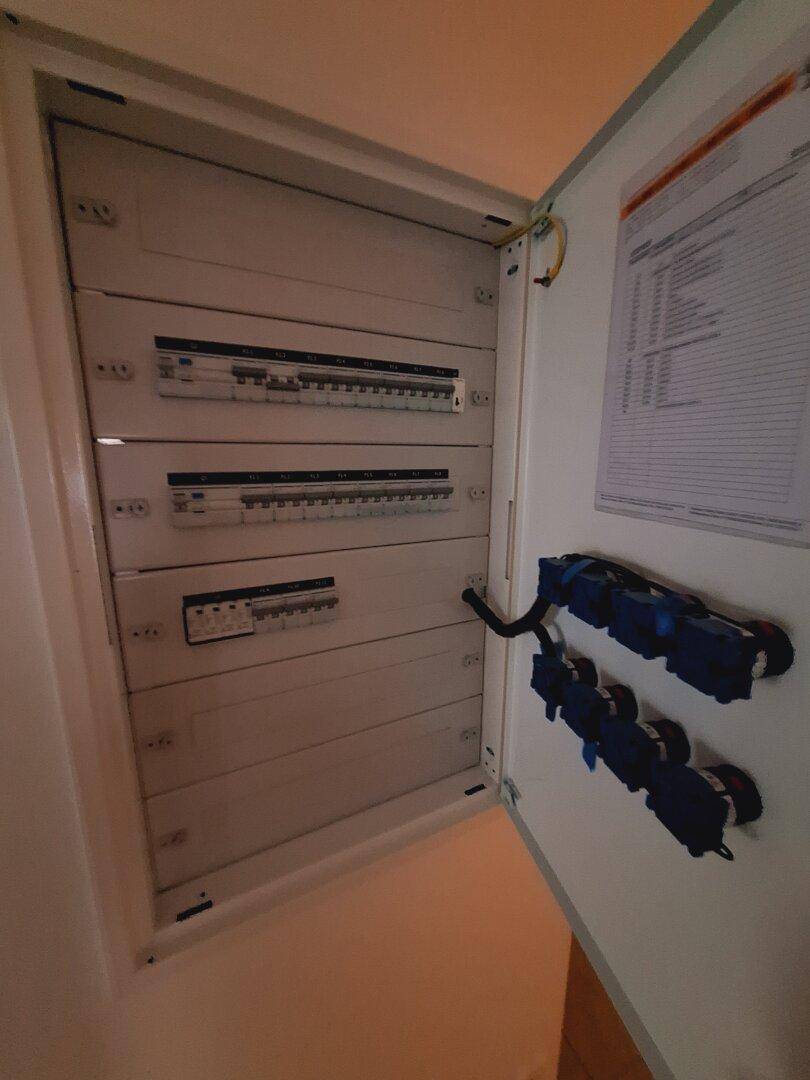 Offener Sicherungskasten mit mehreren Reihen von Schaltern und Verkabelung, ordentlich installiert.
