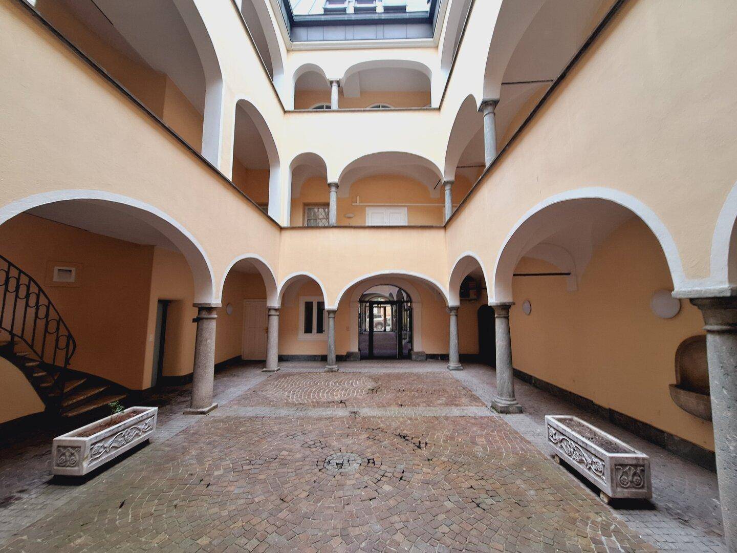 Historischer Innenhof mit Arkaden, Säulen und einem rustikalen Kopfsteinpflasterboden, der eine charmante Atmosphäre bietet.