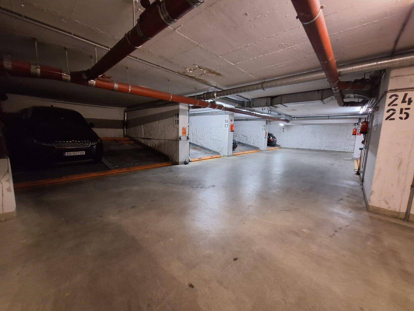 Weitere Ansicht der Tiefgarage mit mehreren Parkplätzen und Hebebühnen für Autos.