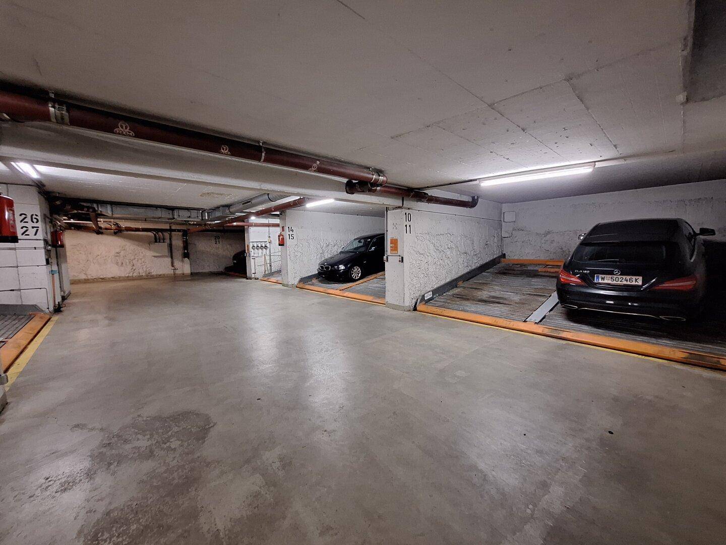 Übersicht der Tiefgarage mit weiteren Parkplätzen und Fahrzeugen auf Hebebühnen.