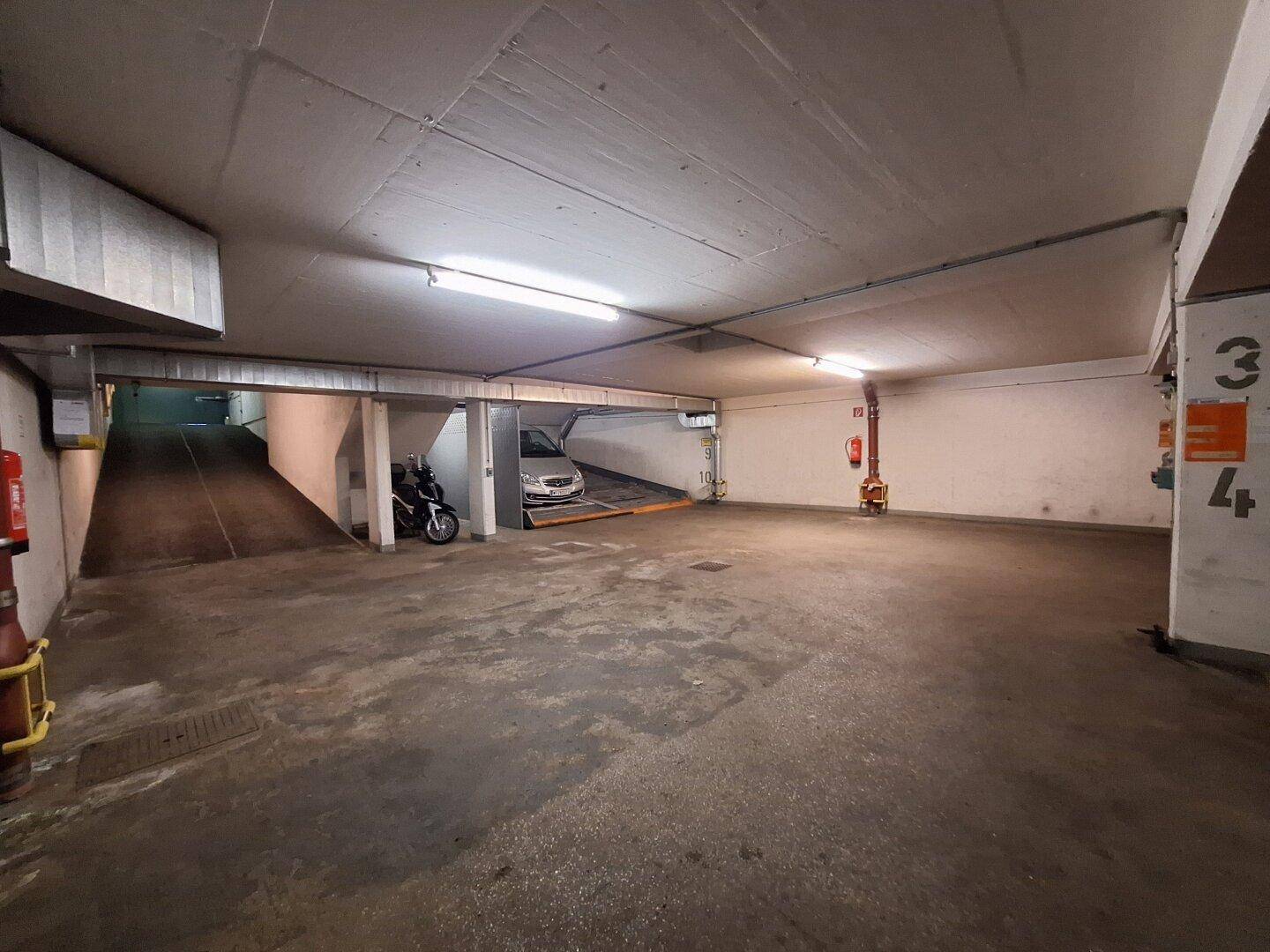 Geräumige Tiefgarage mit Zufahrtsrampe und hydraulischen Parksystemen für mehrere Fahrzeuge.