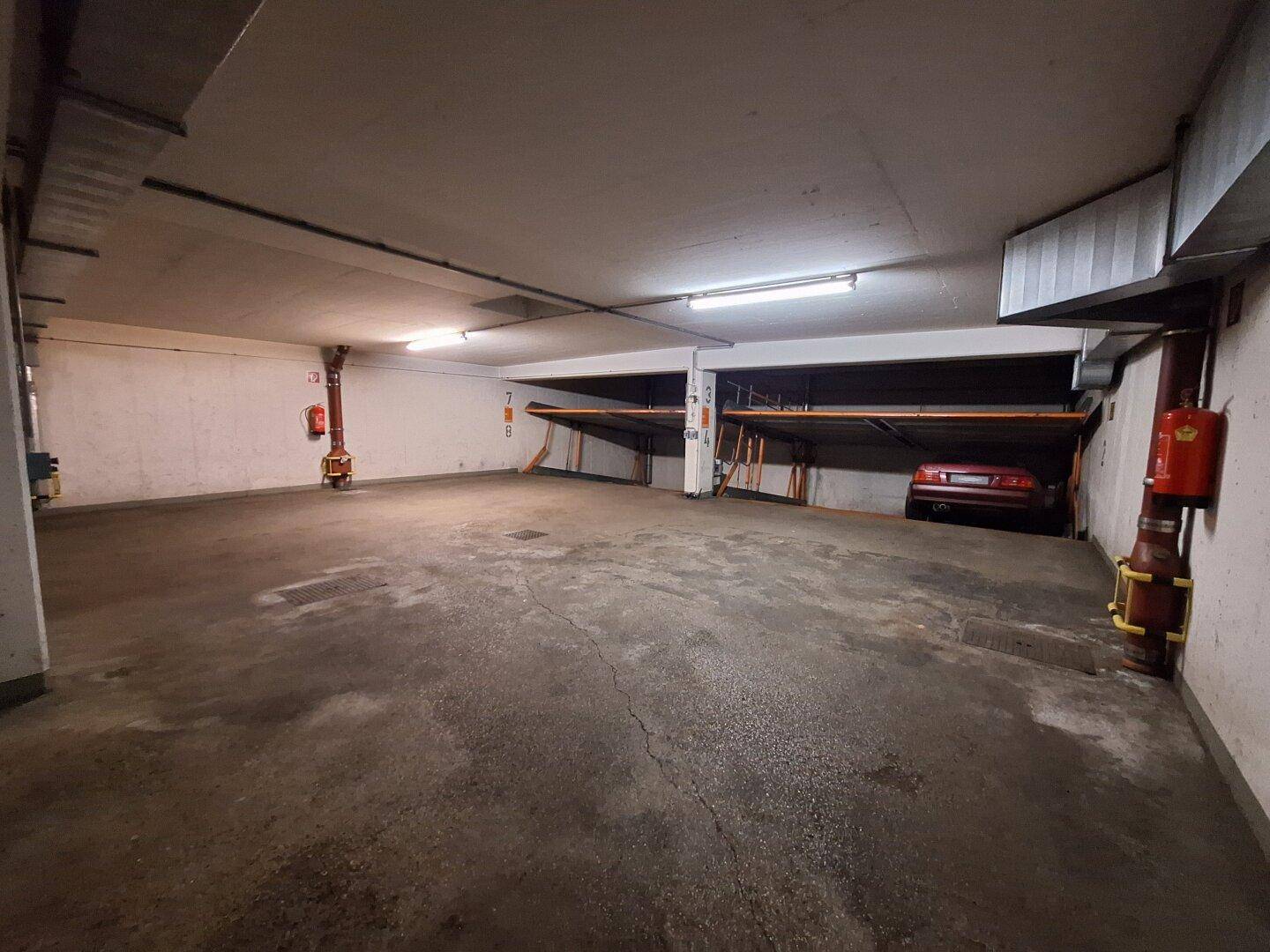 Weitläufige Tiefgarage mit mehreren hydraulischen Parksystemen und einem roten Fahrzeug auf einer Plattform.