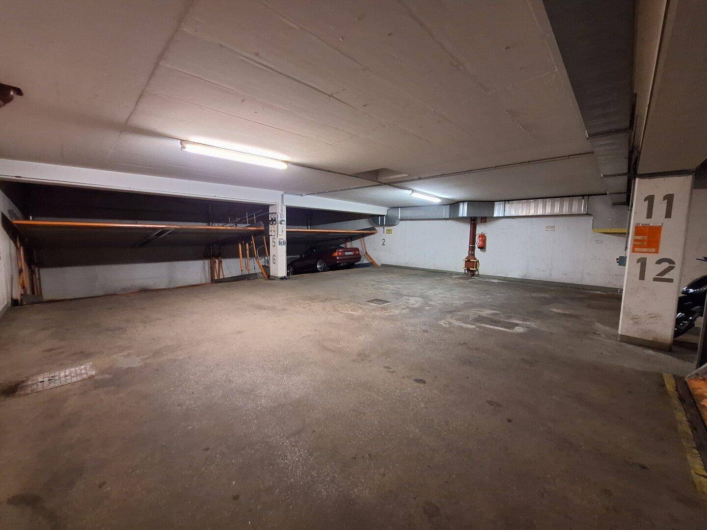 Tiefgarage mit nummerierten Stellplätzen und hydraulischen Parksystemen für Fahrzeuge in einem Wohngebäude.