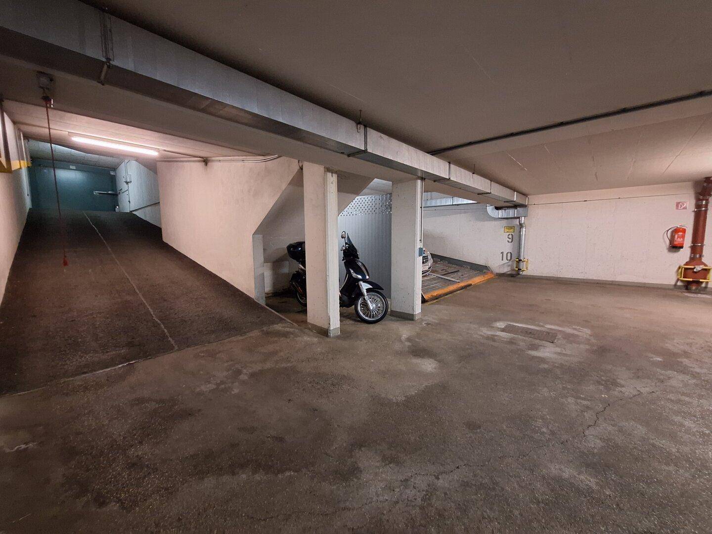 Tiefgarage mit Zufahrtsrampe, Säulen und hydraulischen Parksystemen für Fahrzeuge in einem urbanen Umfeld.