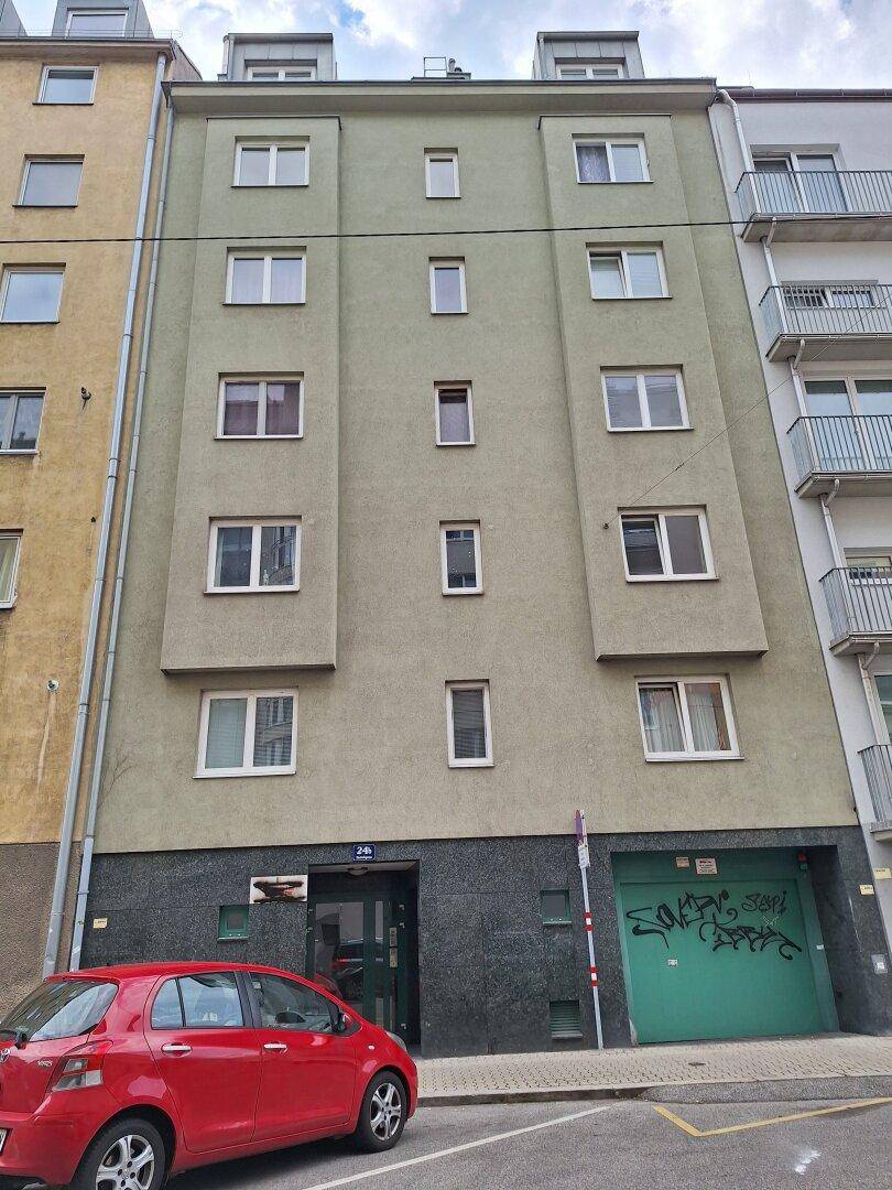 Mehrstöckiges Wohngebäude mit grüner Fassade, vielen Fenstern und einer roten Limousine davor geparkt.