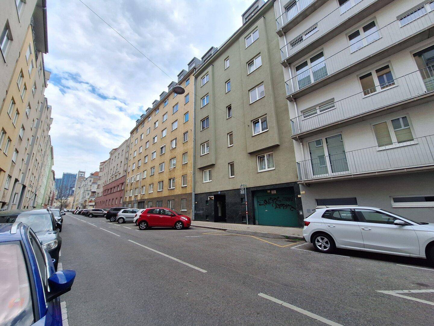Wohngebäude in einer städtischen Umgebung mit parkenden Autos und einer grünen Fassade entlang der Straße.