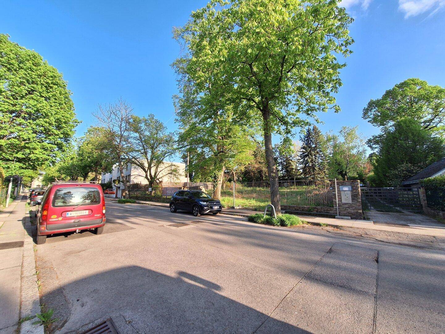 Weitläufige Straßenansicht des Grundstücks mit parkenden Autos und viel Grün.