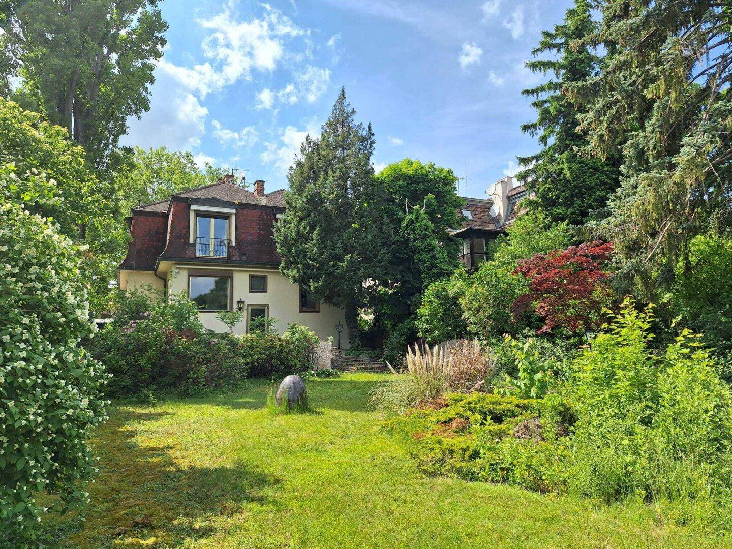Rückansicht des Hauses mit weitläufigem Garten, umgeben von altem Baumbestand und viel Grün.