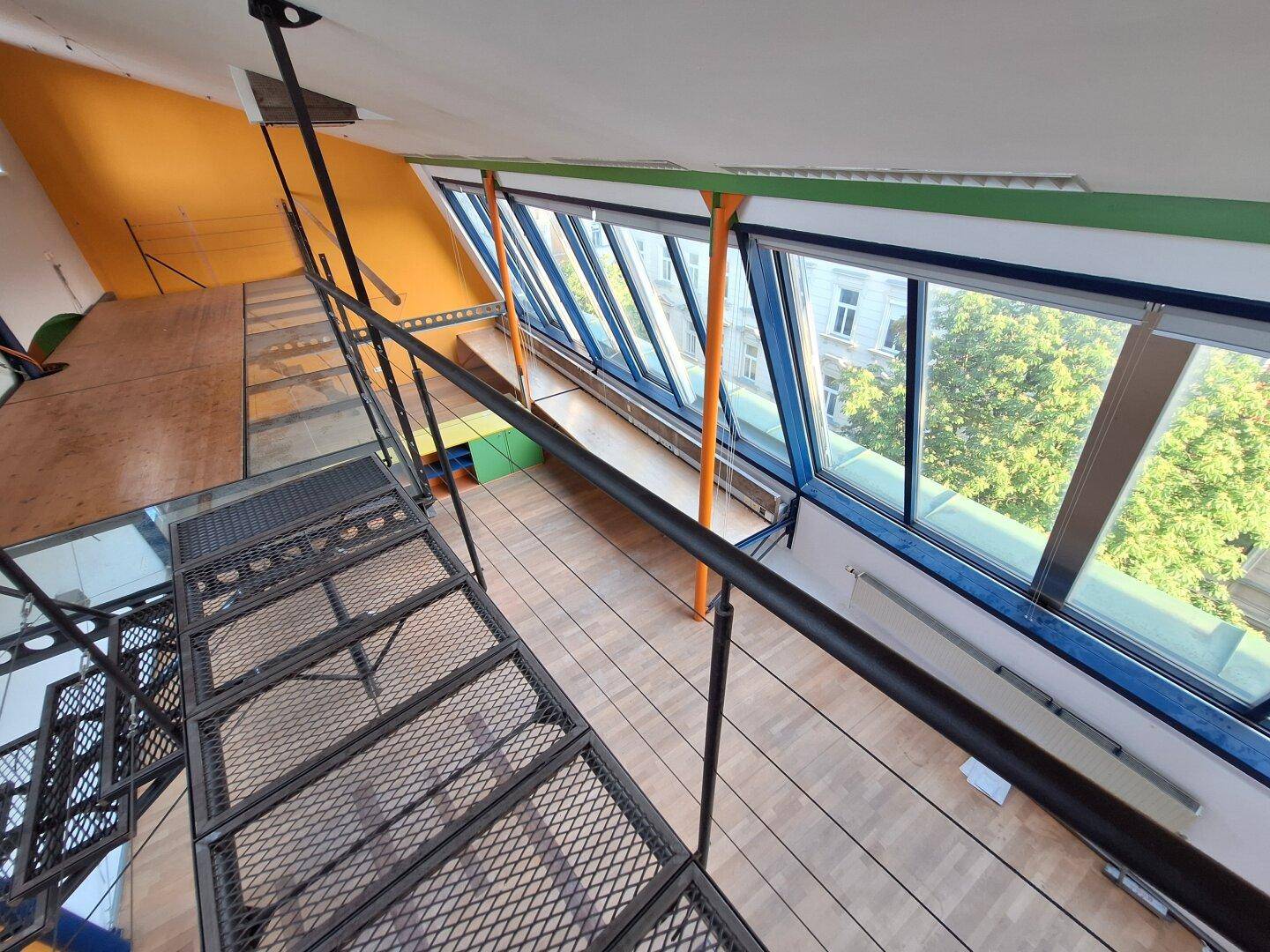 Blick von oben auf einen hellen Büroraum mit Schrägfenstern und Metalltreppe.