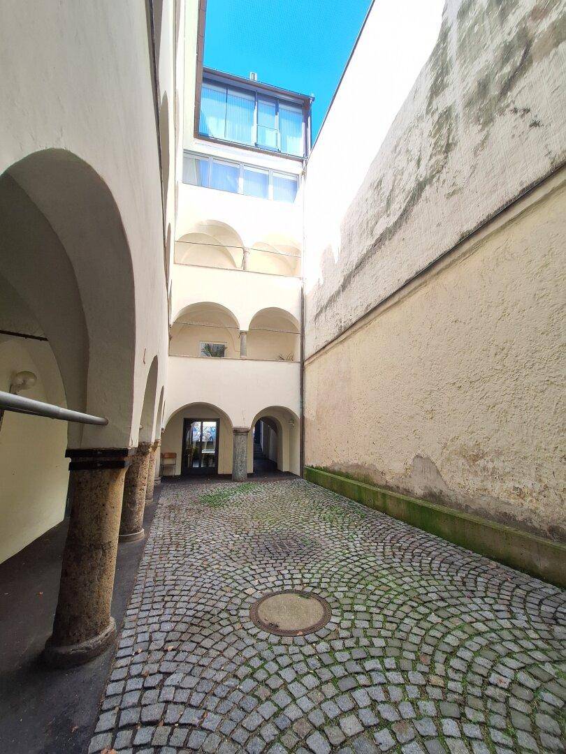 Historischer Innenhof mit Kopfsteinpflaster, umgeben von alten Gebäudefassaden und gewölbten Durchgängen.