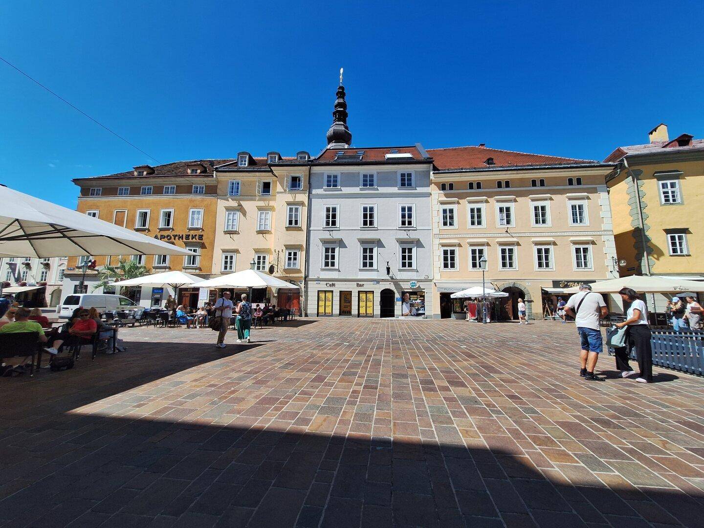 Belebtes Stadtzentrum mit historischen Gebäuden, Außencafés und Menschen unter blauem Himmel.