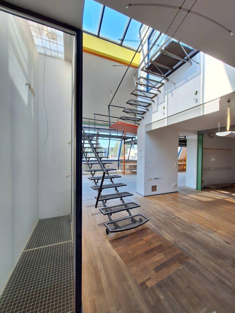 Heller, offener Büroraum mit Holzboden, farbigen Akzenten und einer markanten Wendeltreppe.