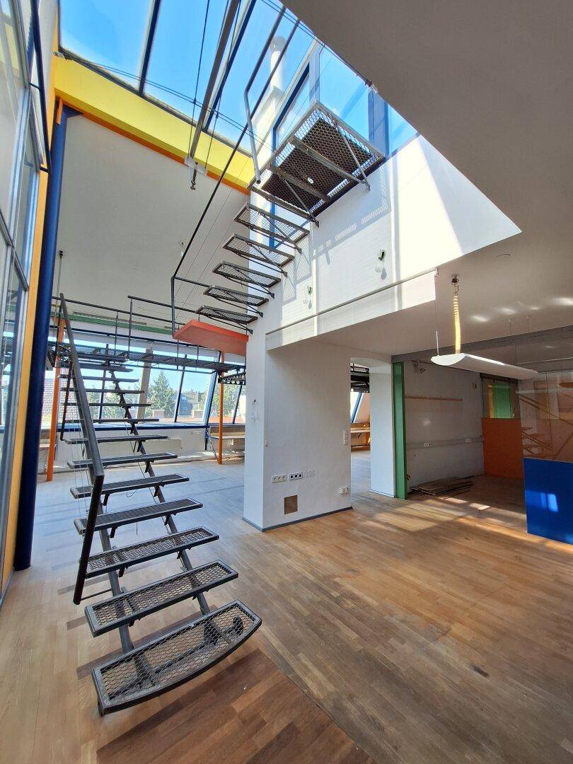 Offener Büroraum mit Holzboden, farbigen Wänden und einer markanten Metalltreppe, die nach oben führt.