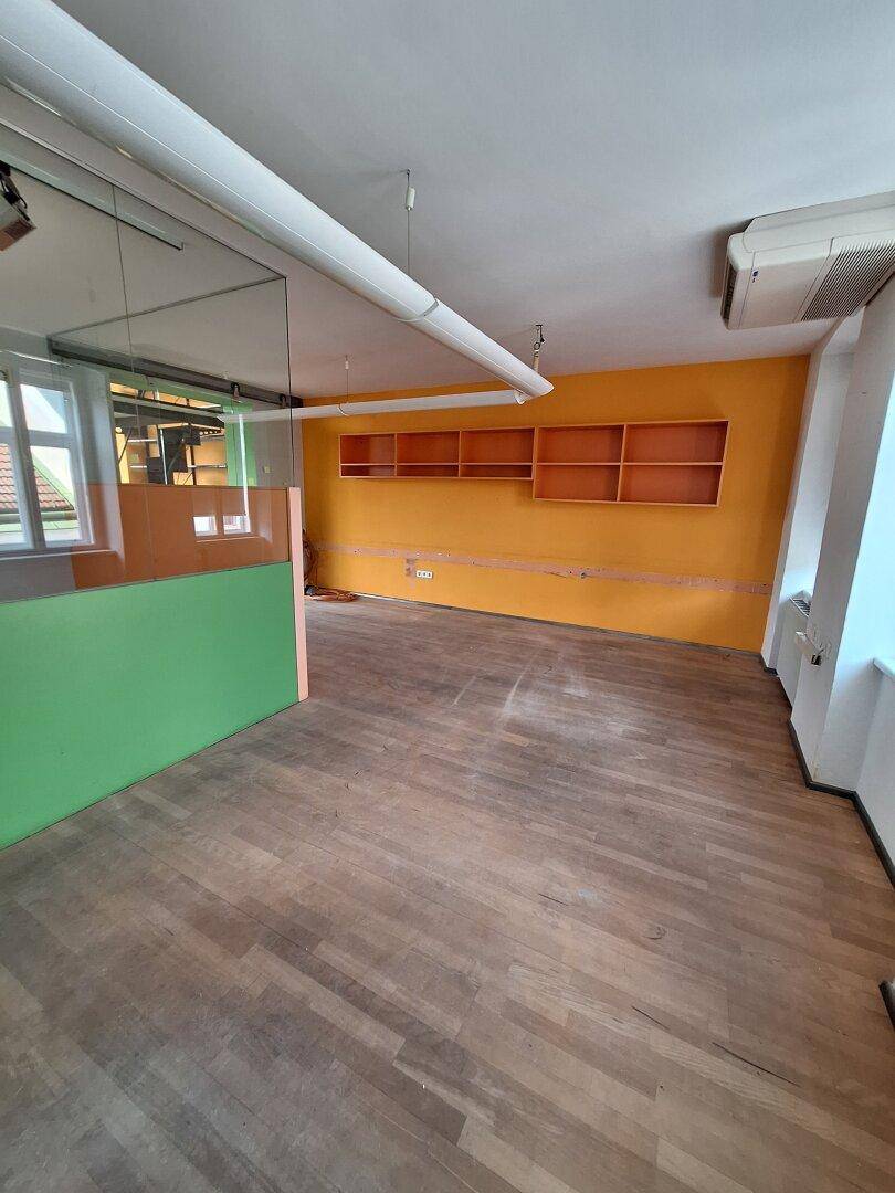 Büroraum mit Holzboden, orangefarbener Akzentwand und integrierten Regalen, gut beleuchtet.