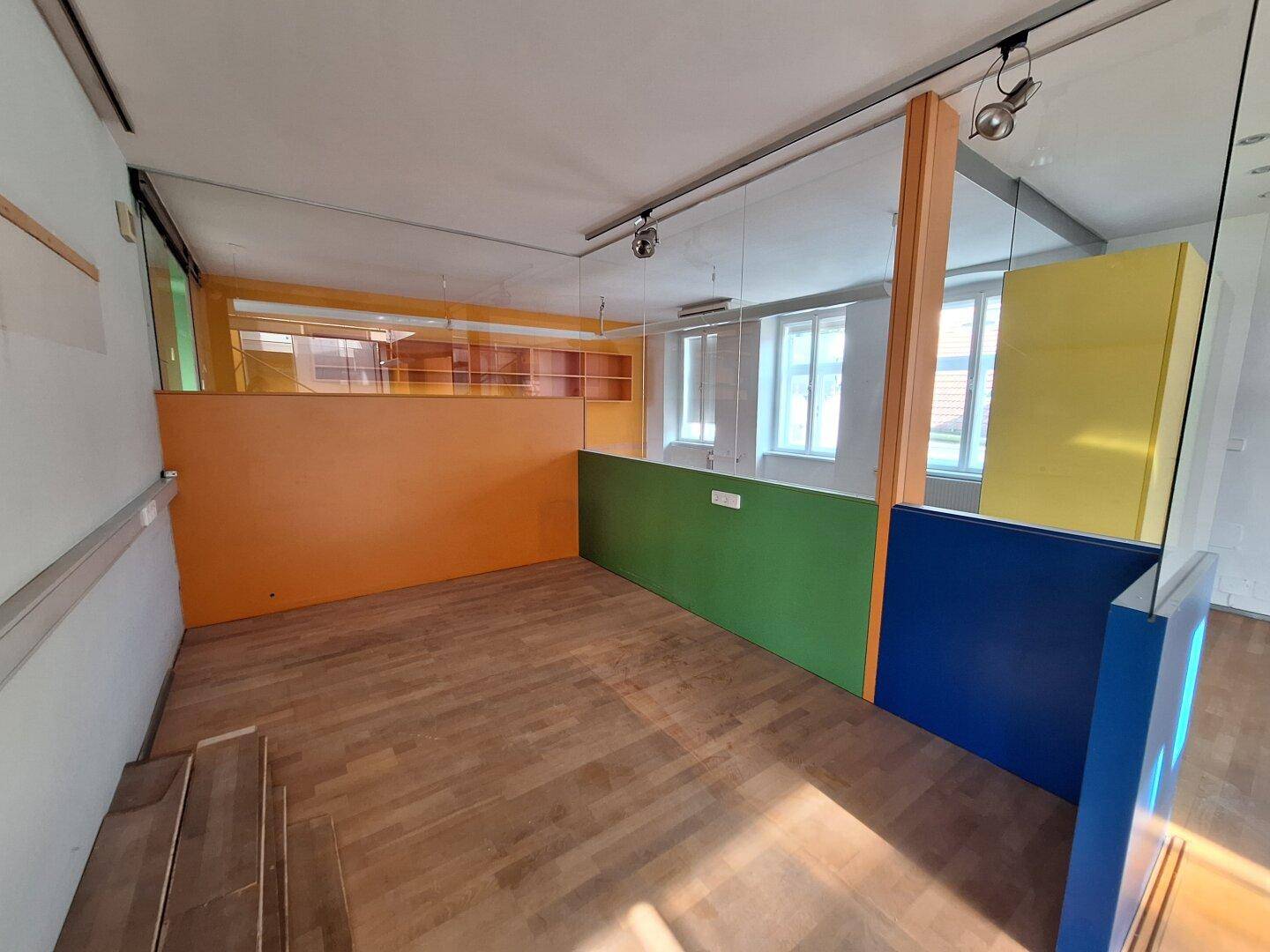 Büroraum mit Holzboden, bunten Trennwänden und Glasabtrennungen, die für eine offene Atmosphäre sorgen.