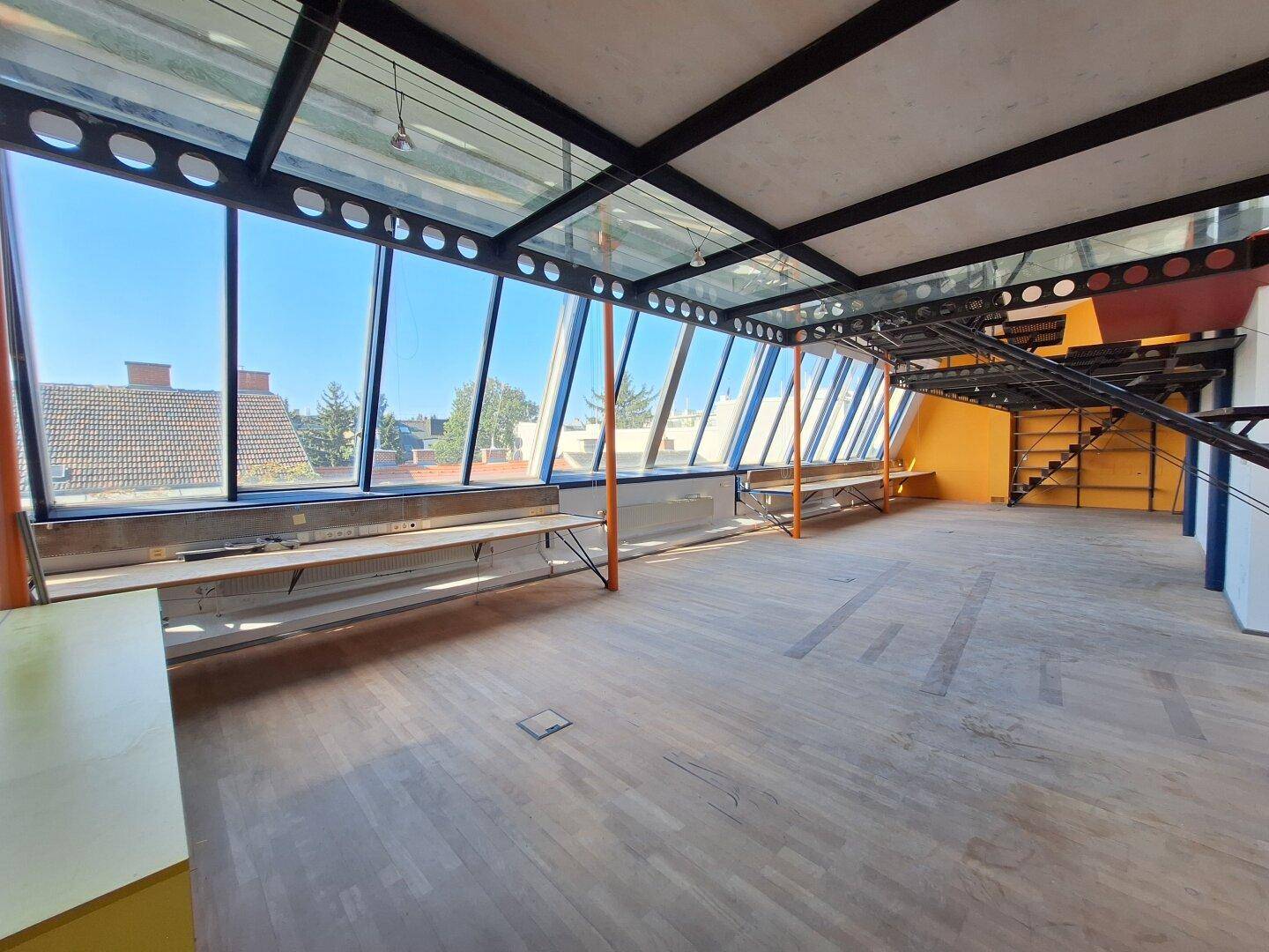 Weitläufiger Büroraum mit Holzboden, schrägen Glasfenstern und Blick auf die Dächer der Umgebung.