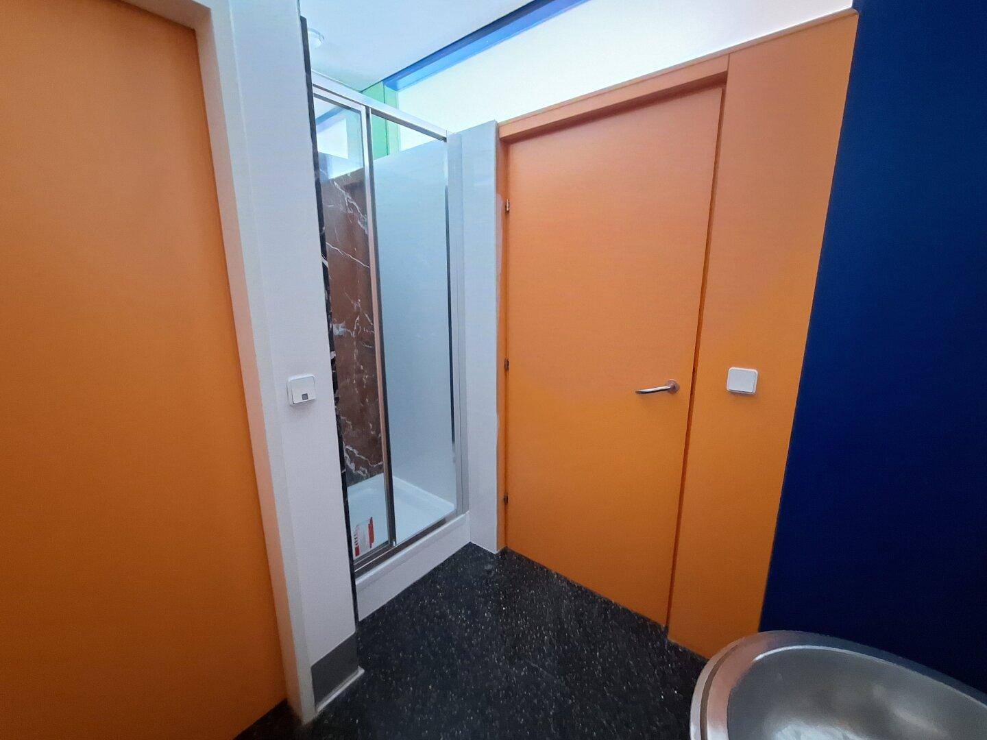 Modernes Badezimmer mit dunklem Fliesenboden, Duschkabine und orangefarbener Tür.