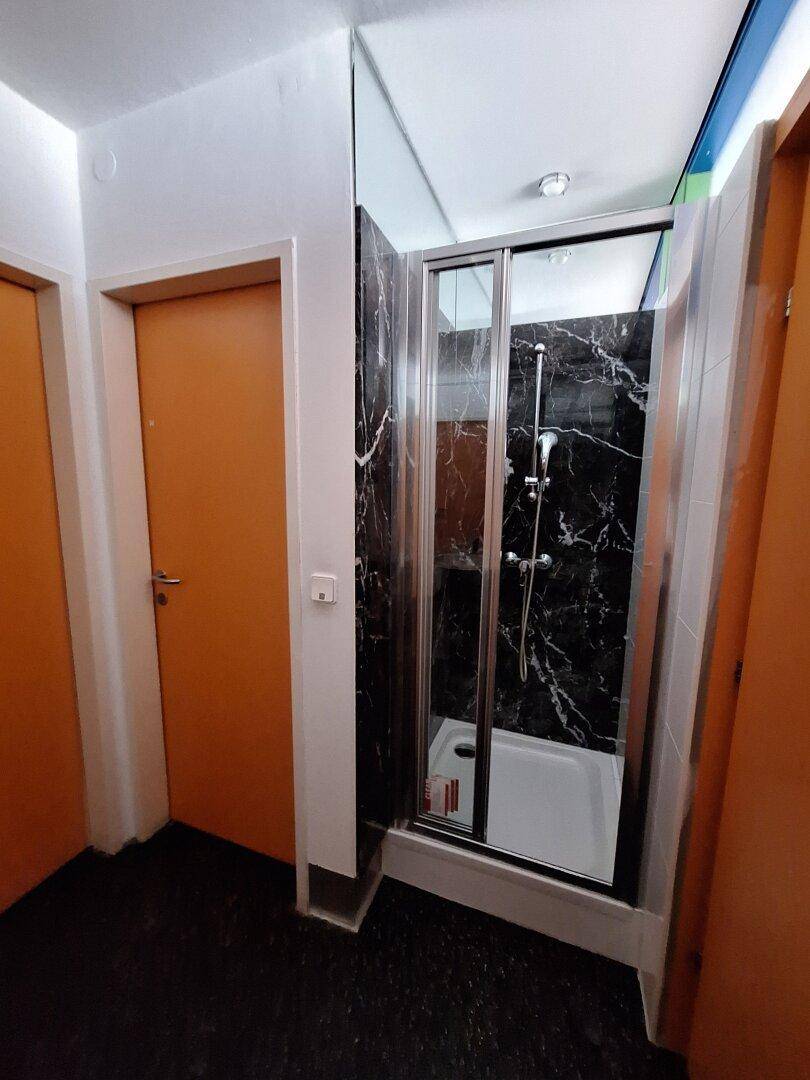 Badezimmer mit einer modernen Duschkabine, schwarzen Marmorfliesen und orangefarbenen Türen.