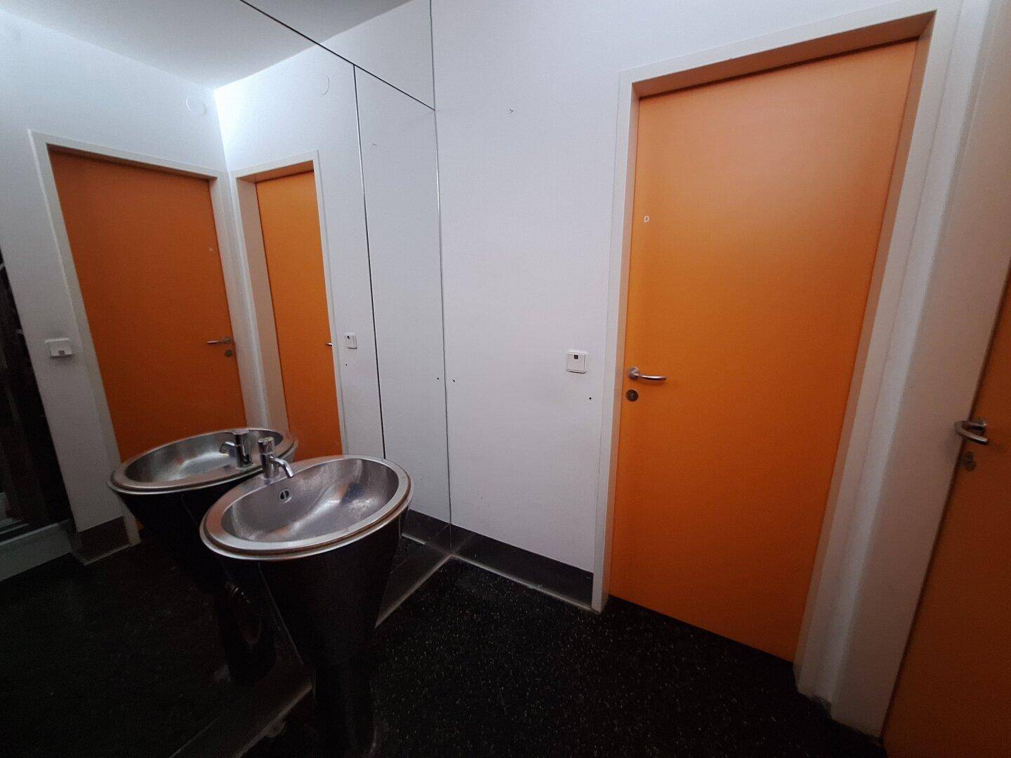 Badezimmer mit zwei Waschbecken, dunklem Fliesenboden und orangefarbenen Türen.