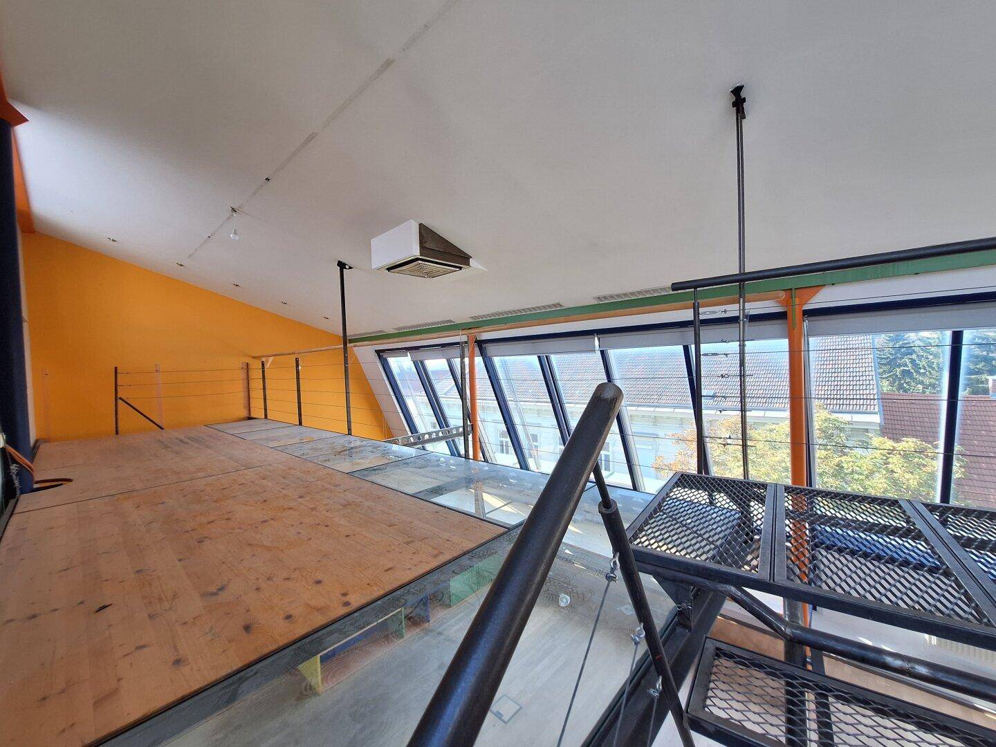 Geräumiger Loftbereich mit einer Holz- und Glasempore, großen Fenstern und Blick auf die Umgebung.