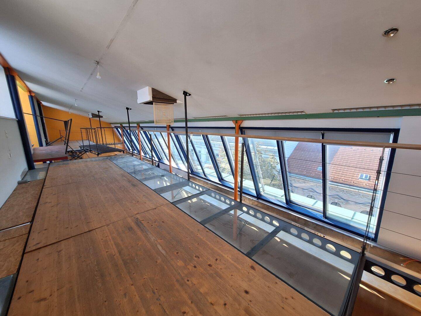 Heller Loftbereich mit Holzempore und einer langen Fensterfront, die viel natürliches Licht hereinlässt.