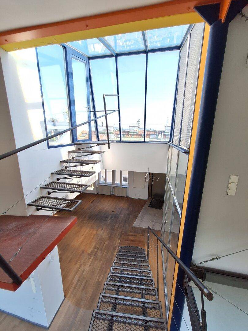 Offenes Treppenhaus mit Metallstufen und einer beeindruckenden Glasdachkonstruktion, die den Raum erhellt.