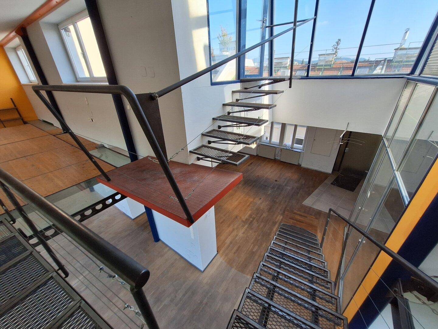 Geräumiger Wohnbereich mit offener Metalltreppe und Holzboden, der zu den oberen Ebenen führt.