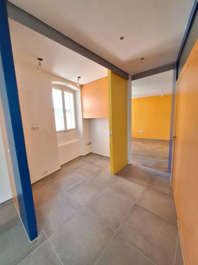Kleiner Raum mit Fliesenboden, einem Fenster und orangefarbenen Hängeschränken.