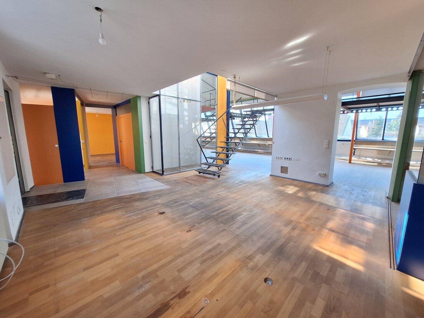 Großer Wohnbereich mit Parkettboden, offener Treppe und farbigen Akzentwänden in einem Loftambiente.